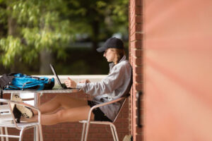 A female college student sits at an outdoor table, working on her laptop.
